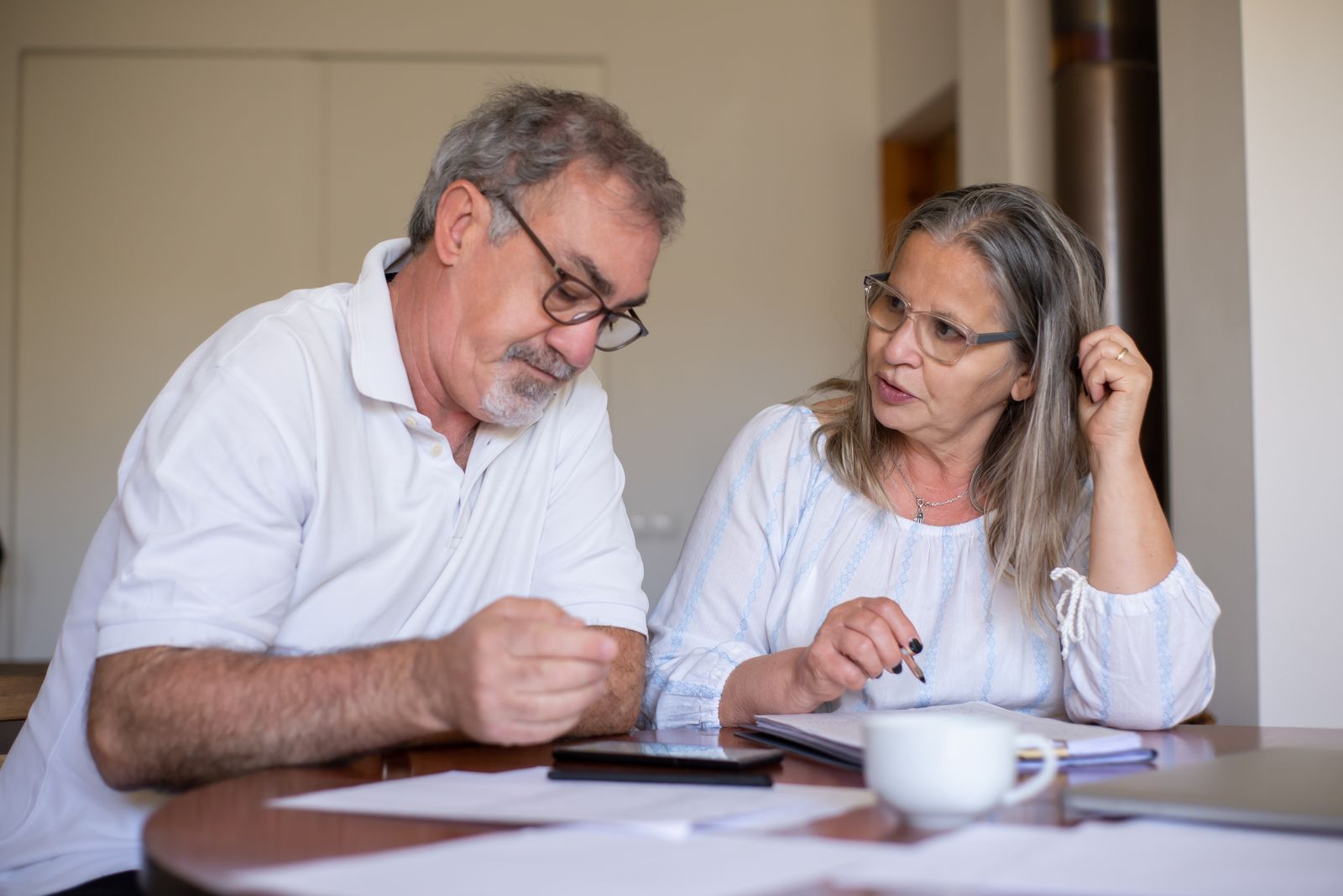 A woman in her seventies at her kitchen counter, reading a letter beside the family photo wall